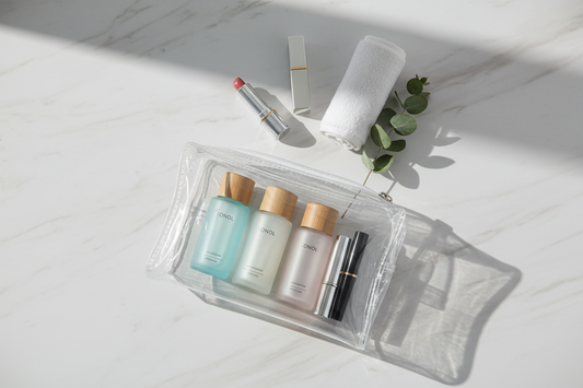 Trousse de toilette transparente avec flacons de voyage organisés sur marbre blanc – style éditorial minimaliste